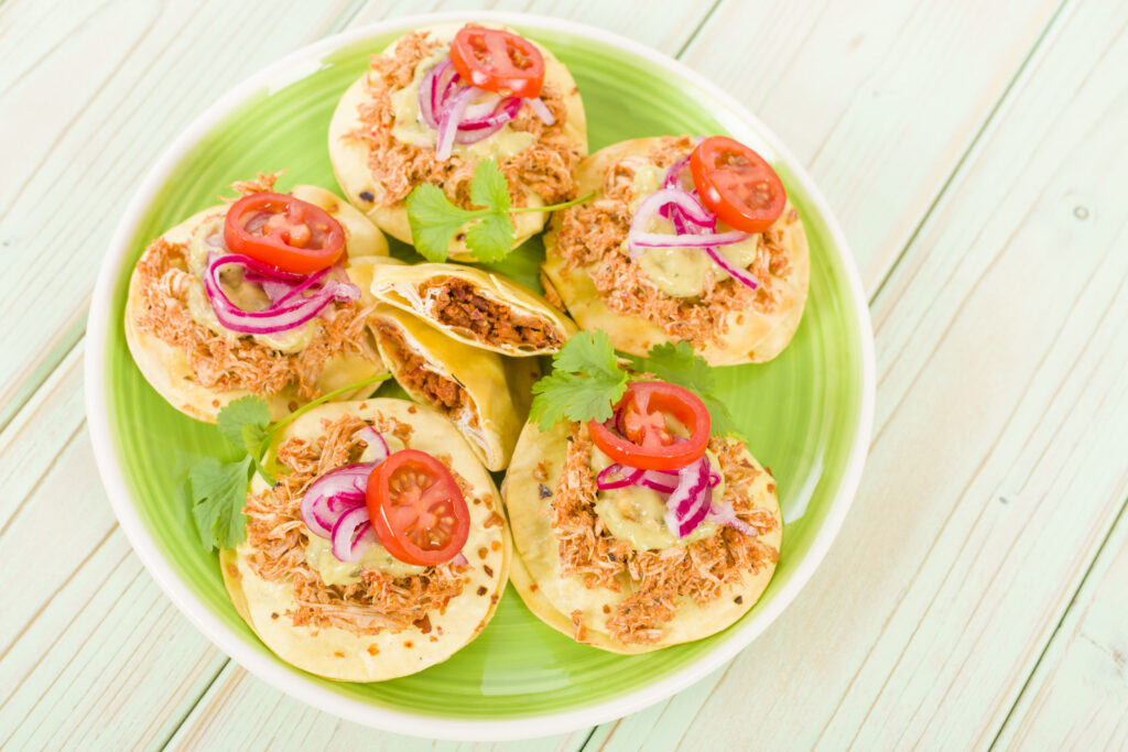 Tostadas topped with shredded meat, tomatoes, and herbs on a green plate