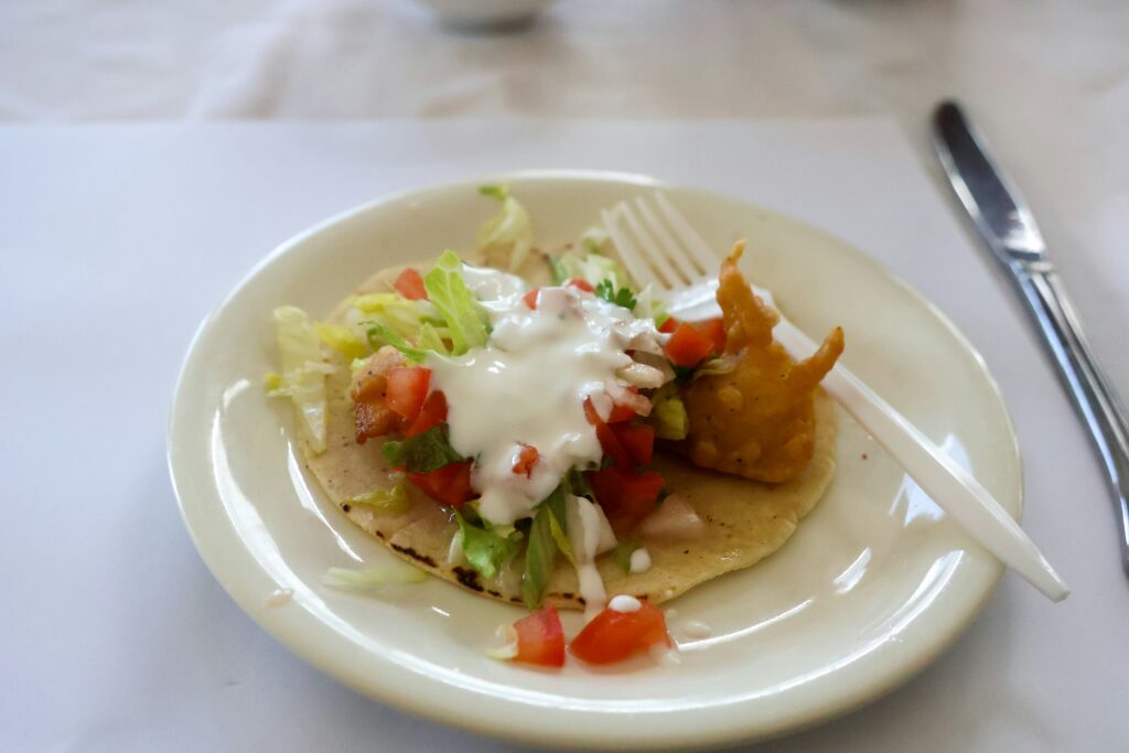 Small taco topped with lettuce, tomatoes, and white sauce on a plate