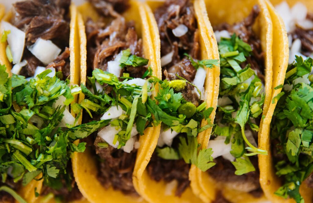 Close-up of corn tortilla tacos filled with shredded beef, chopped onions, and fresh cilantro.