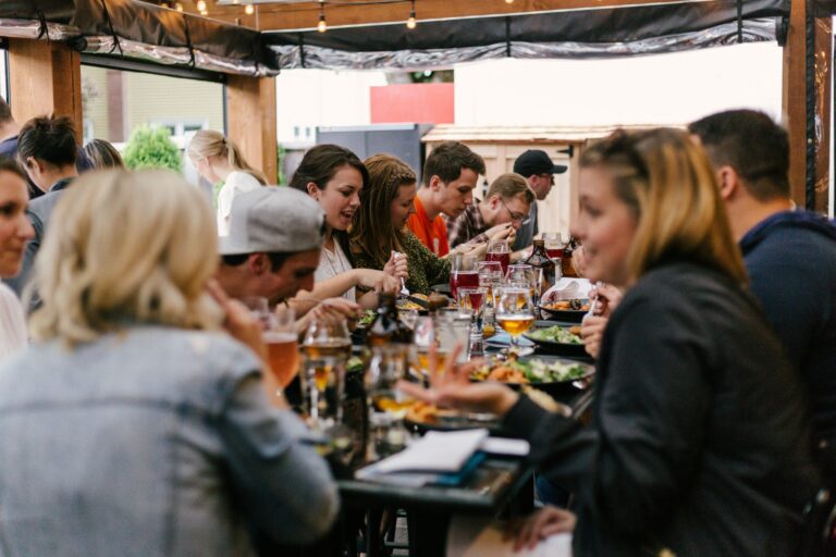 Group of people dining together at a long table in a casual restaurant, sharing food and conversation.