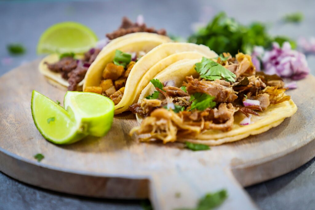 Close-up of assorted street tacos with lime wedges and fresh toppings on a wooden board.